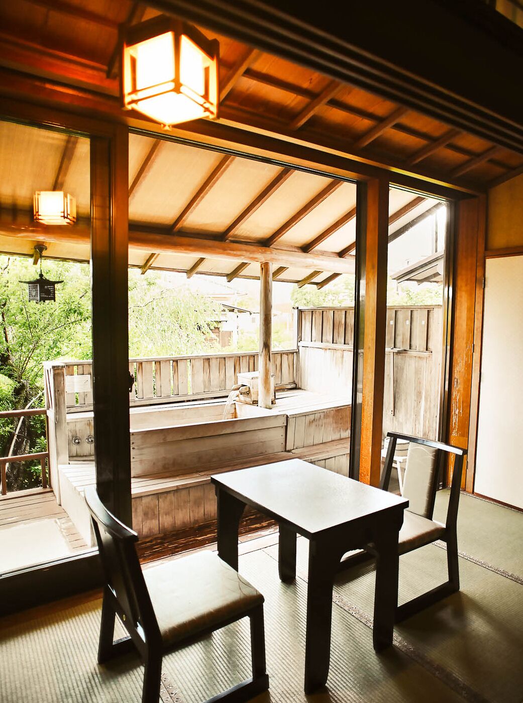 A covered outdoor seating area with wooden benches and tables, large windows, and a wooden deck.