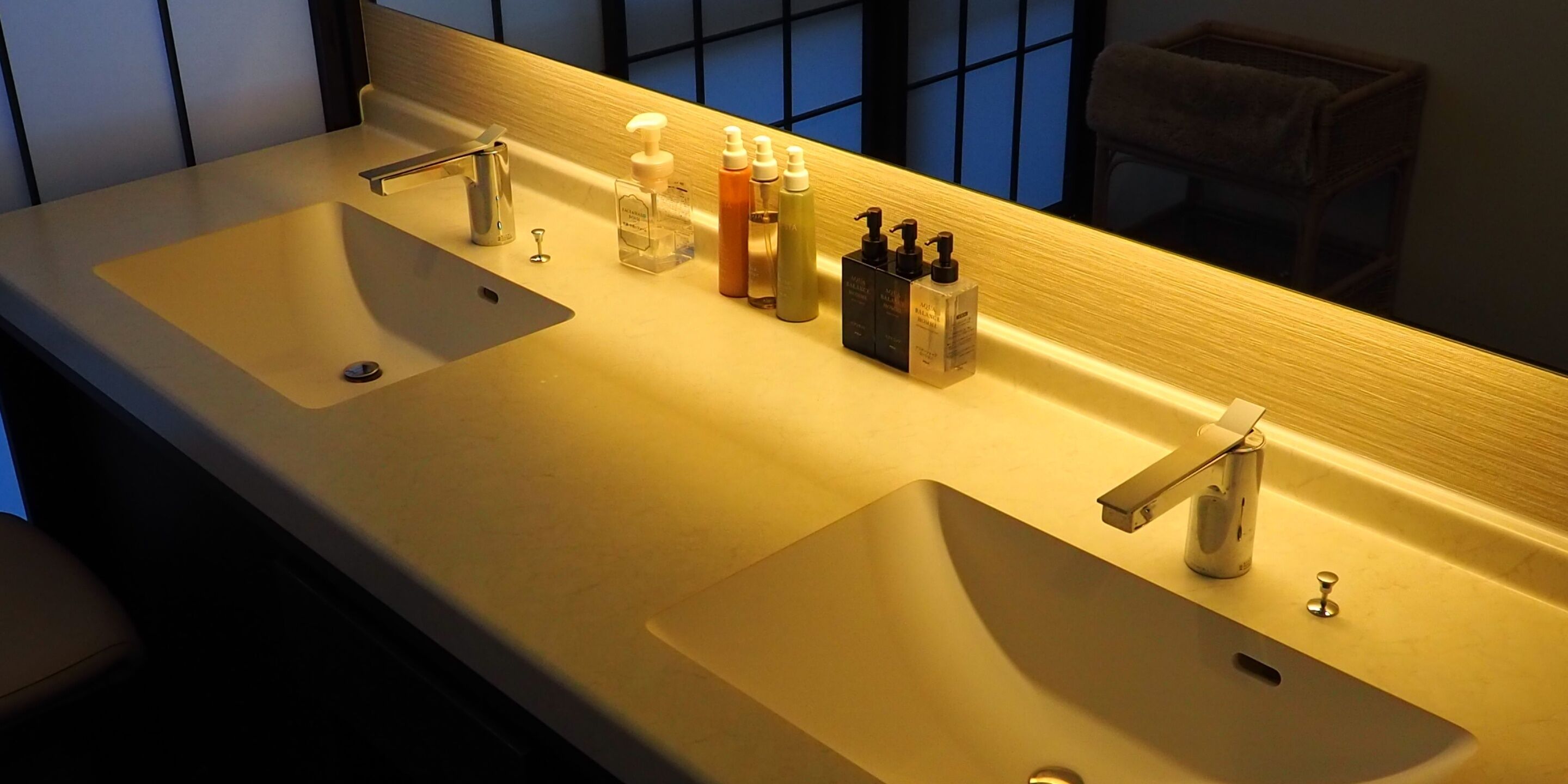 Un baño con dos lavamanos, un espejo y distintos artículos de aseo.