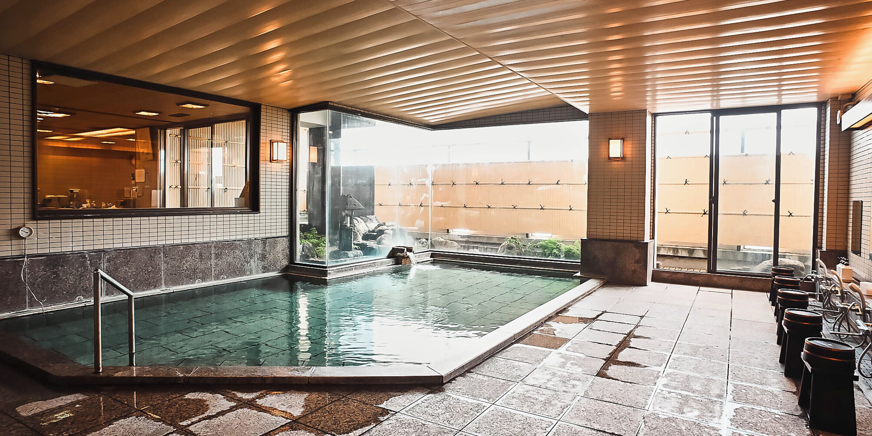 A hotel room with a large indoor pool, a view of the city, and a seating area with tables and chairs.