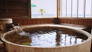 A wooden hot tub with a waterfall feature, set against a wooden wall and a window with a view of the ocean. - Shin Kado Ya (Atami)