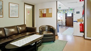 A reception area with a leather sofa, a small armchair, a bulletin board with notices, and a fire extinguisher. - Bed's Rumsuthyrning (Norrköping)