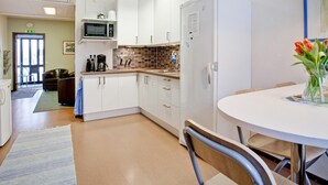 A modern kitchen with white cabinets, a microwave, and a refrigerator. There is a dining table with chairs and a vase of flowers. - Bed's Rumsuthyrning (Norrköping)