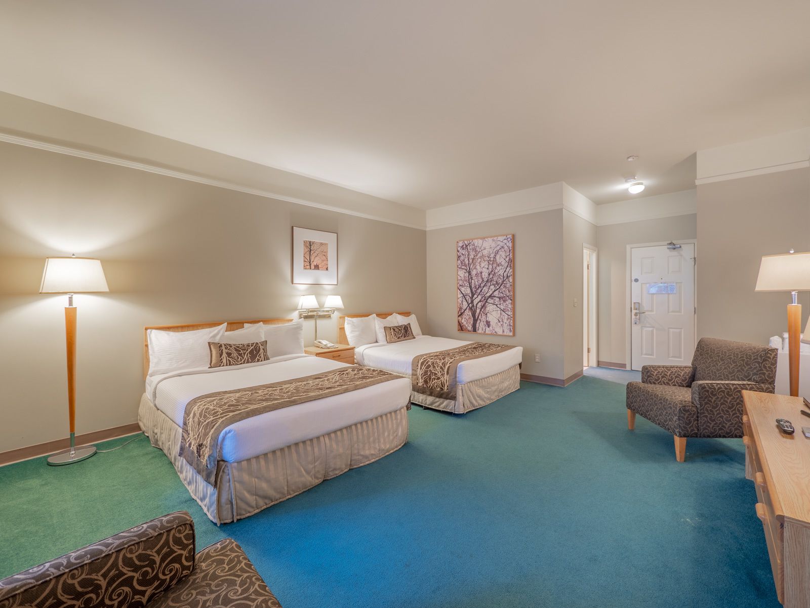 A hotel room with two beds, a desk, a chair, and a door.