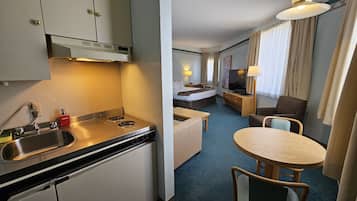 Ein kompaktes Hotelzimmer mit Küchenzeile, einem Bett, einem kleinen Schreibtisch, einem Fernseher und einer Sitzecke.