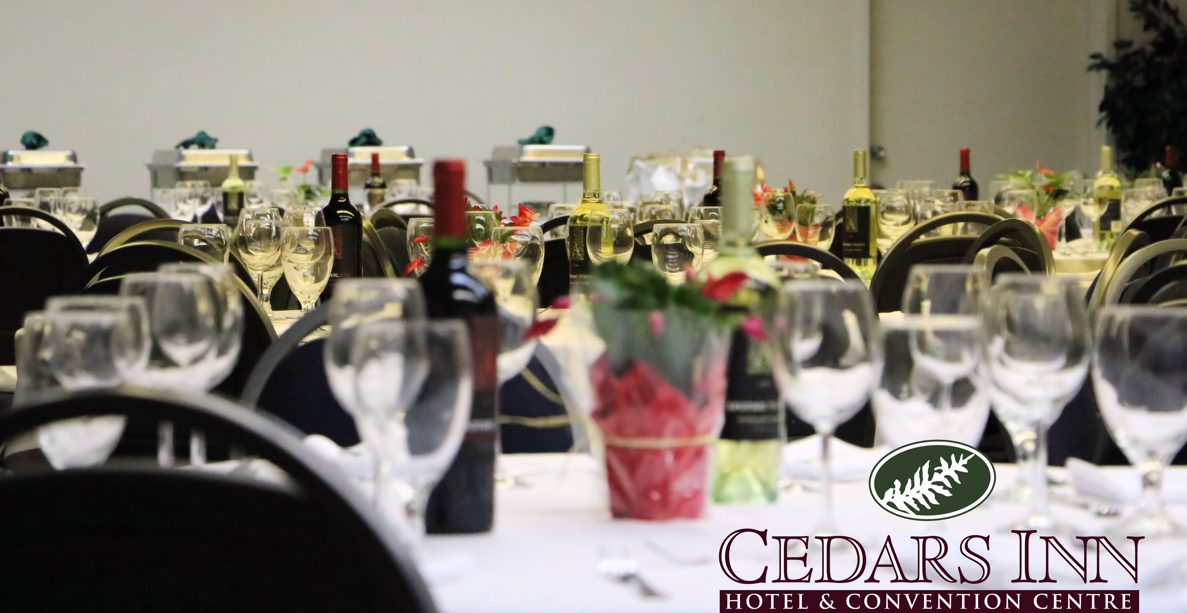Una mesa dispuesta para un evento formal en el Hotel Cedars Inn & Convention Centre, con copas de vino, botellas y centros de mesa florales.
