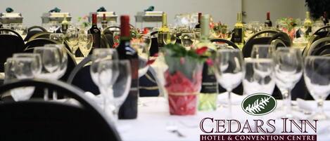Una mesa dispuesta para un evento formal en el Hotel Cedars Inn & Convention Centre, con copas de vino, botellas y centros de mesa florales.