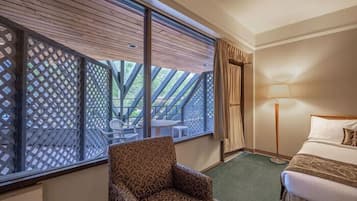 Habitación de hotel con cama, una silla, una mesa y vistas al exterior a través de una ventana con celosía.