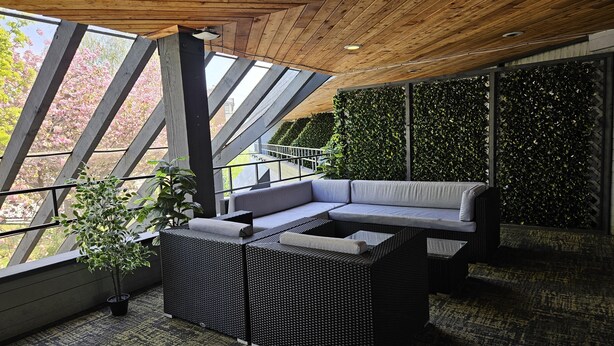 A modern outdoor seating area with a sofa and a table, surrounded by large windows and a green wall. - Cedars Inn Hotel & Convention Center (Gibsons)