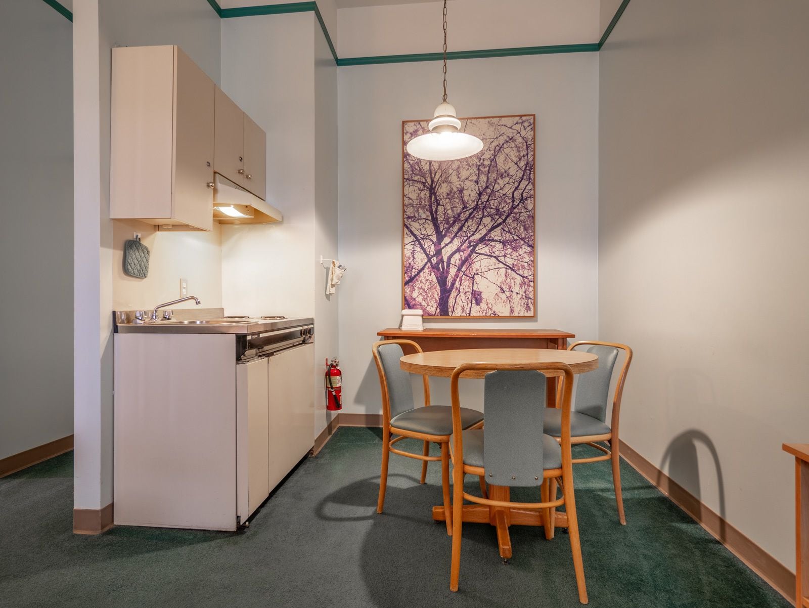 Cocina compacta con comedor, que incluye una mesa y sillas de madera, una lámpara colgante y un extintor de incendios en la pared.
