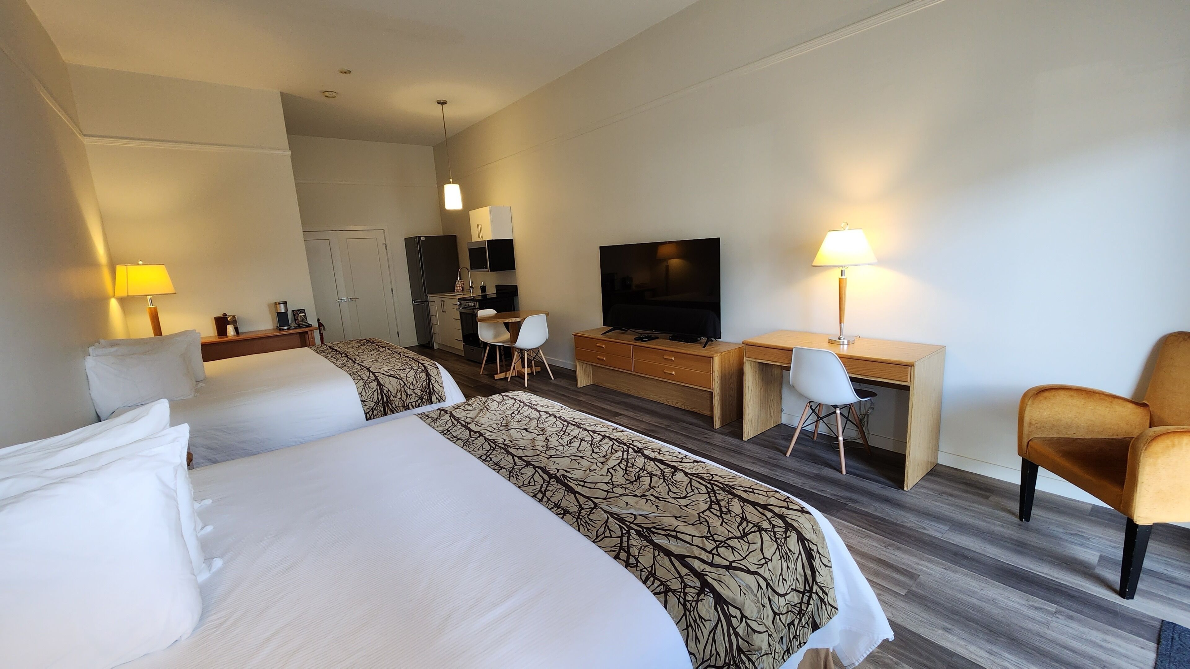 A hotel room with two beds, a desk, a TV, and a chair.