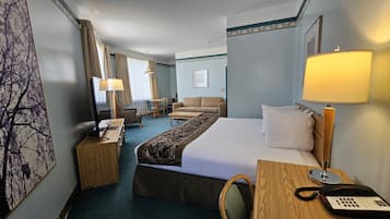 A hotel room with a bed, a desk with a telephone, a chair, a sofa, a table, and a lamp.