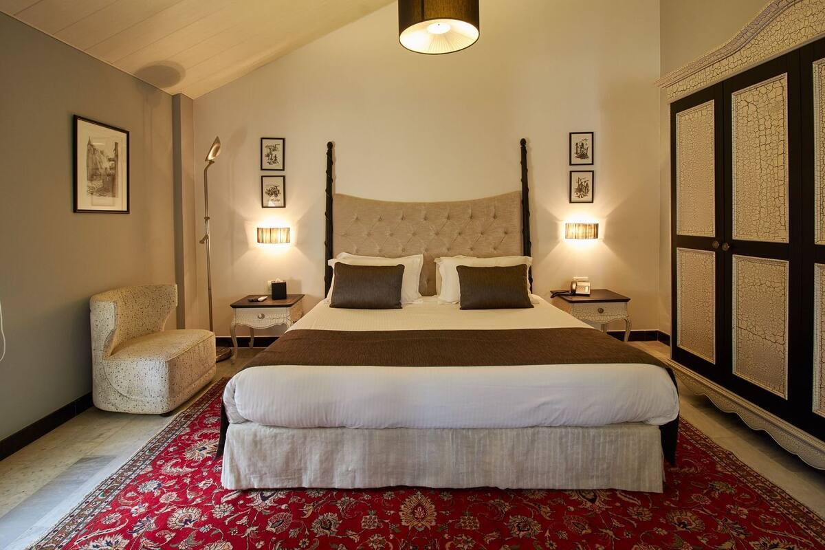 Ein geräumiges Schlafzimmer mit einem großen Bett, einem roten Teppich mit Muster und einer dekorativen Wandverkleidung.