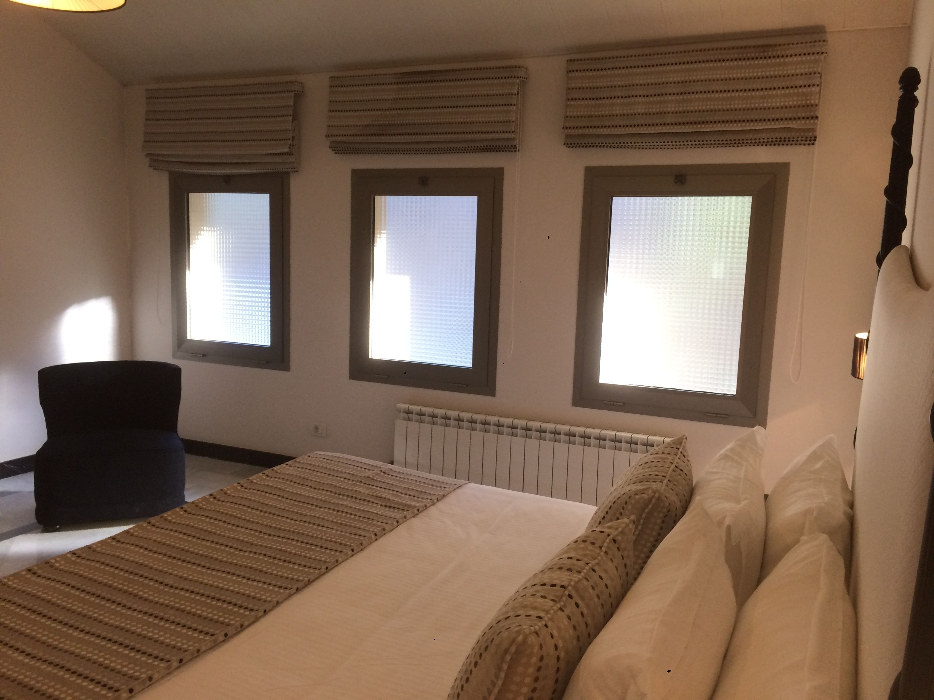 A bedroom with a bed, a chair, and three windows with blinds.