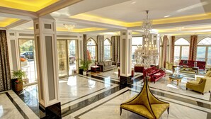 Un hall d’entrée spacieux, doté d’un haut plafond, de lustres et d’un grand espace salon avec des canapés et des fauteuils.