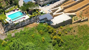 Vue aérienne d’un quartier résidentiel avec un grand bâtiment doté d’une piscine, de panneaux solaires et de terrasses cultivées.