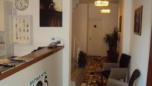 A hotel reception area with a reception desk labeled "BOUTIQUE HOTEL TEOS," a clock, framed photos, a staircase, and a patterned floor. - Teos Hotel (Antalya)