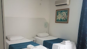A hotel room with two single beds, a small table, a wall-mounted air conditioner, and a painting. - Teos Hotel (Antalya)
