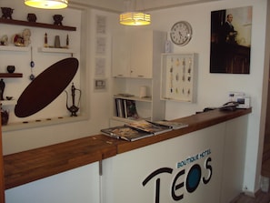 A hotel reception desk with a clock, a framed photo, and a sign that reads 'BOUTIQUE HOTEL TEOS'. - Teos Hotel (Antalya)