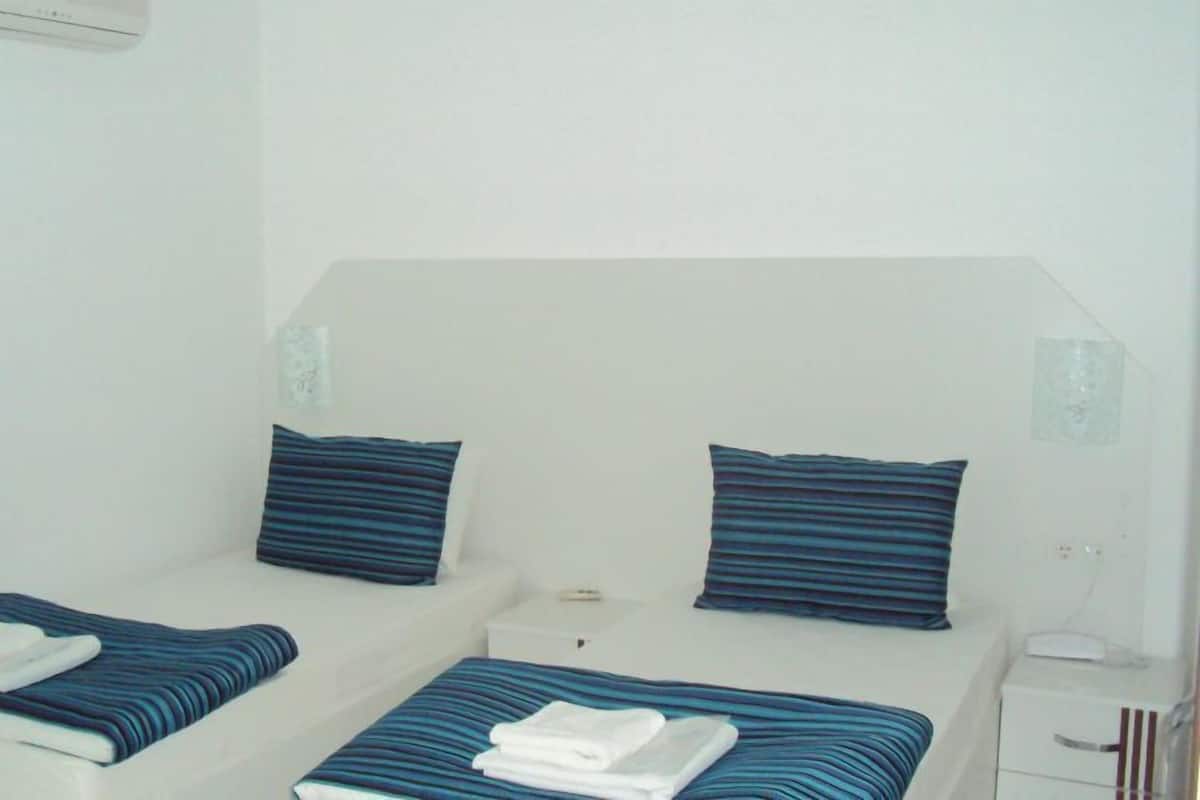 A small, simple room with two beds, each with a striped pillow and a folded towel.