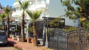 A white multi-story building with balconies, palm trees, and a gated entrance. - Teos Hotel (Antalya)