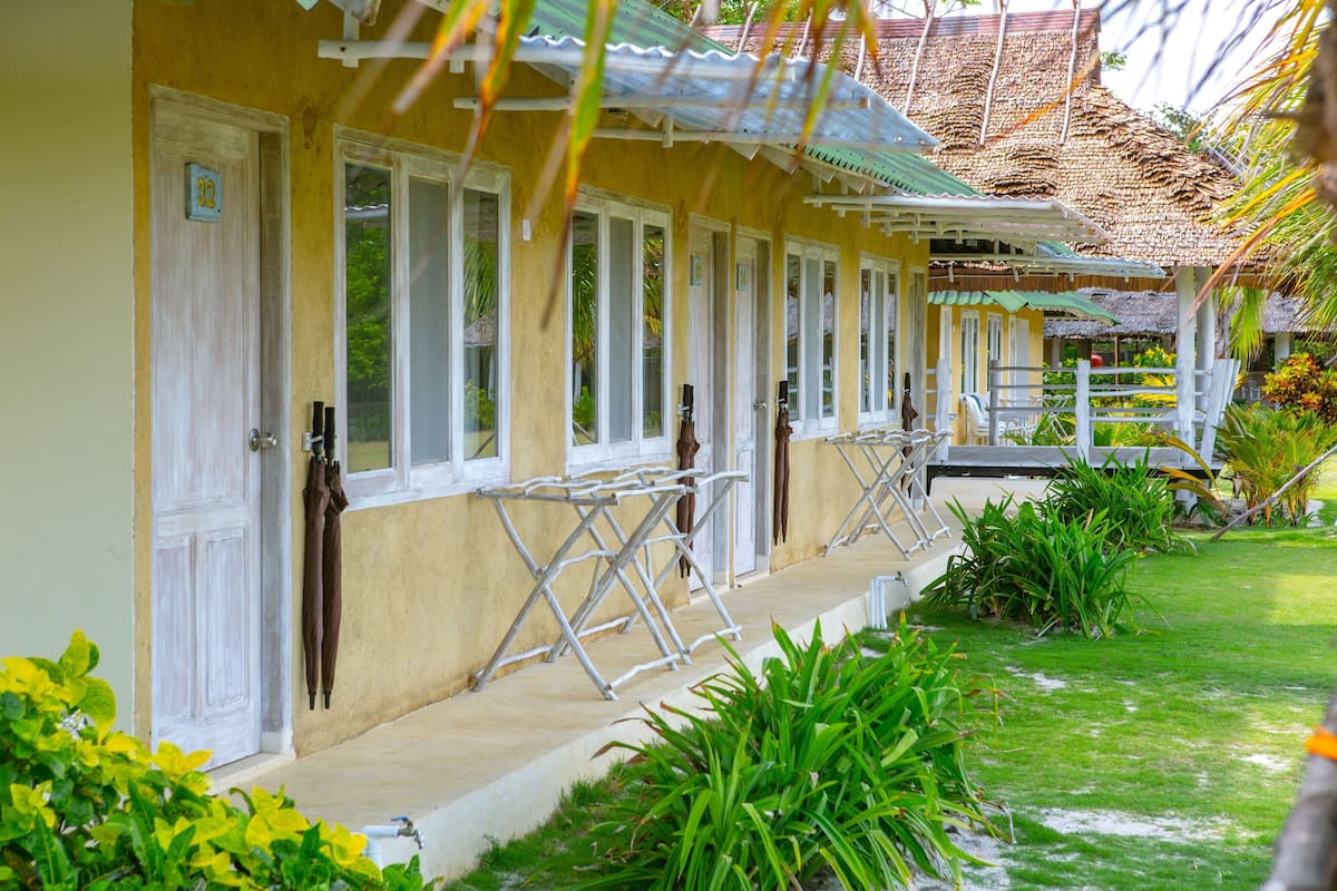 A yellow building with white doors and windows, a covered porch, and a thatched roof.