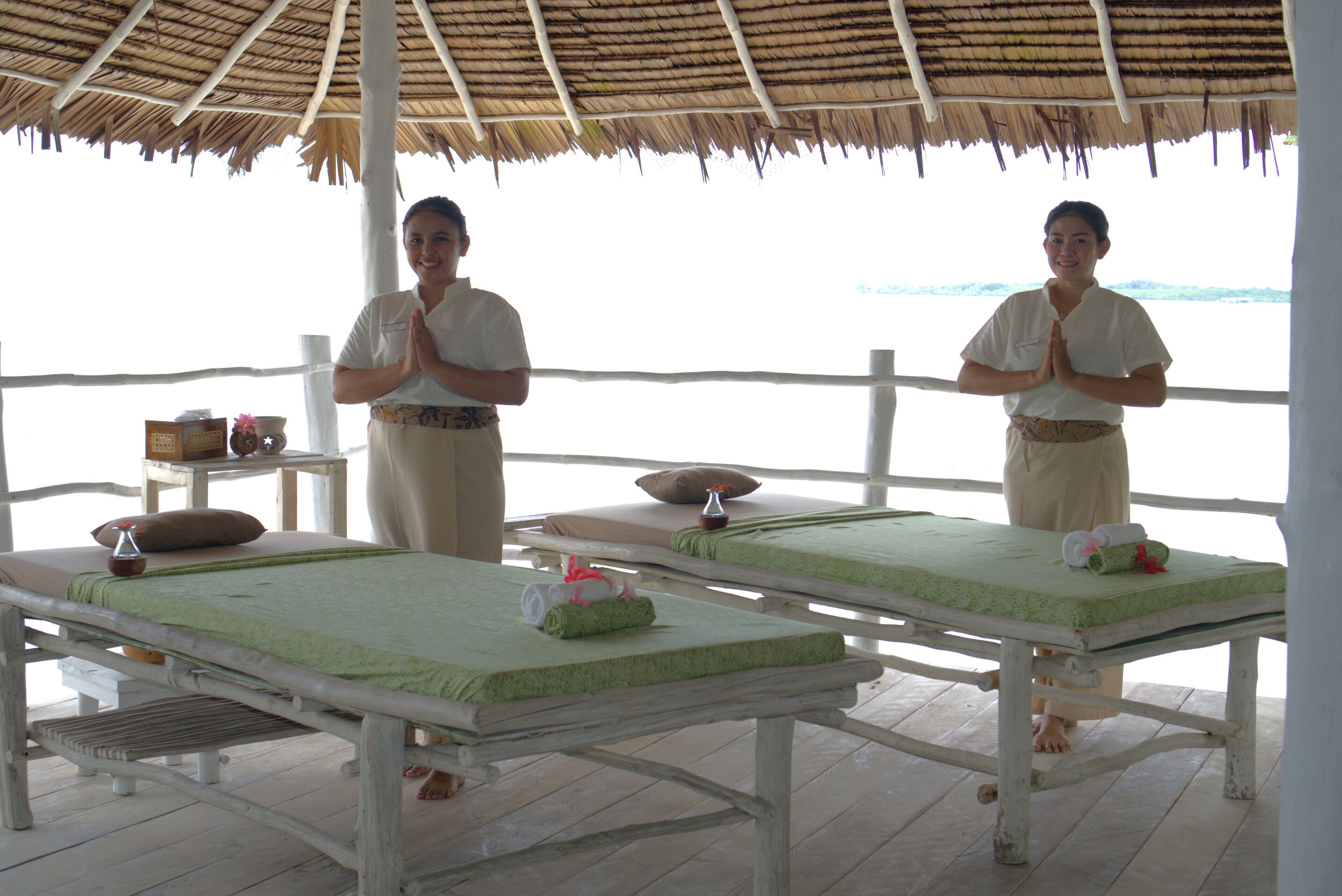 Two massage tables with green mats, a thatched roof, and a wooden floor.