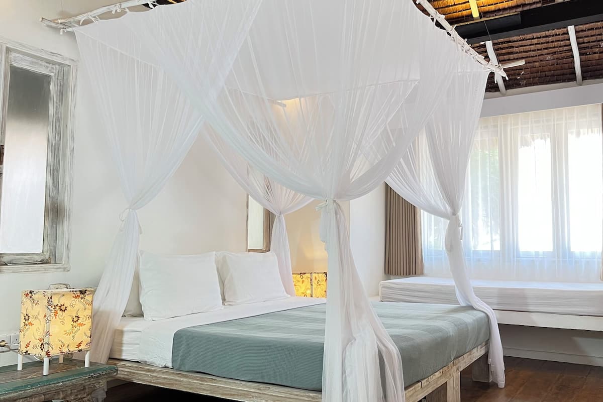 A room with a four-poster bed, a bedside table, a lamp, and a window with curtains.