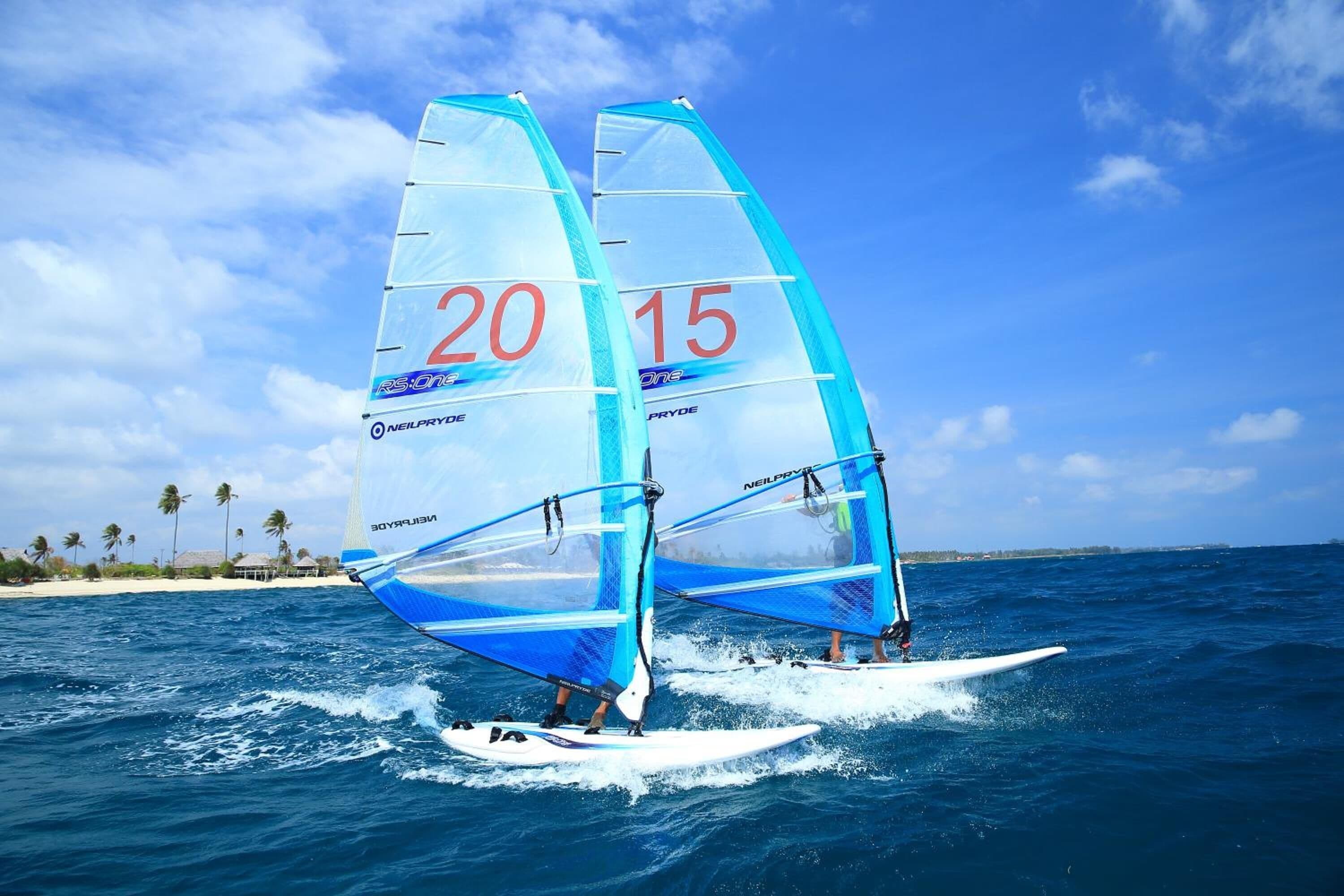 Two windsurfing boards with sails marked "20" and "15" on a clear day over the ocean.