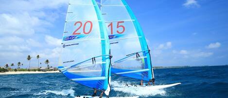 Two windsurfing boards with sails marked "20" and "15" on a clear day over the ocean.