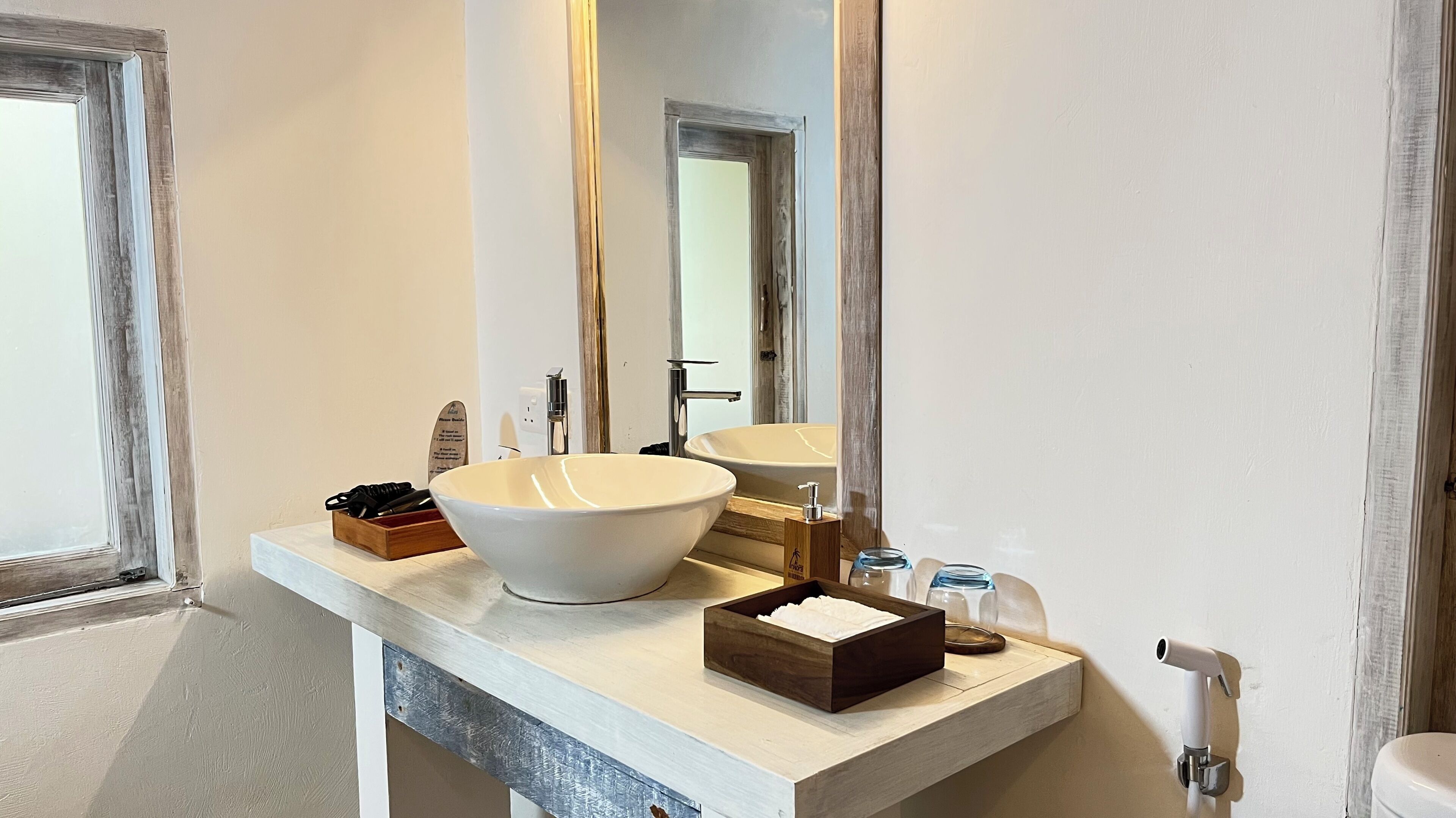 Un baño con un lavamanos blanco de pedestal grande, otro lavamanos más pequeño, un espejo y una caja de madera sobre el mostrador.