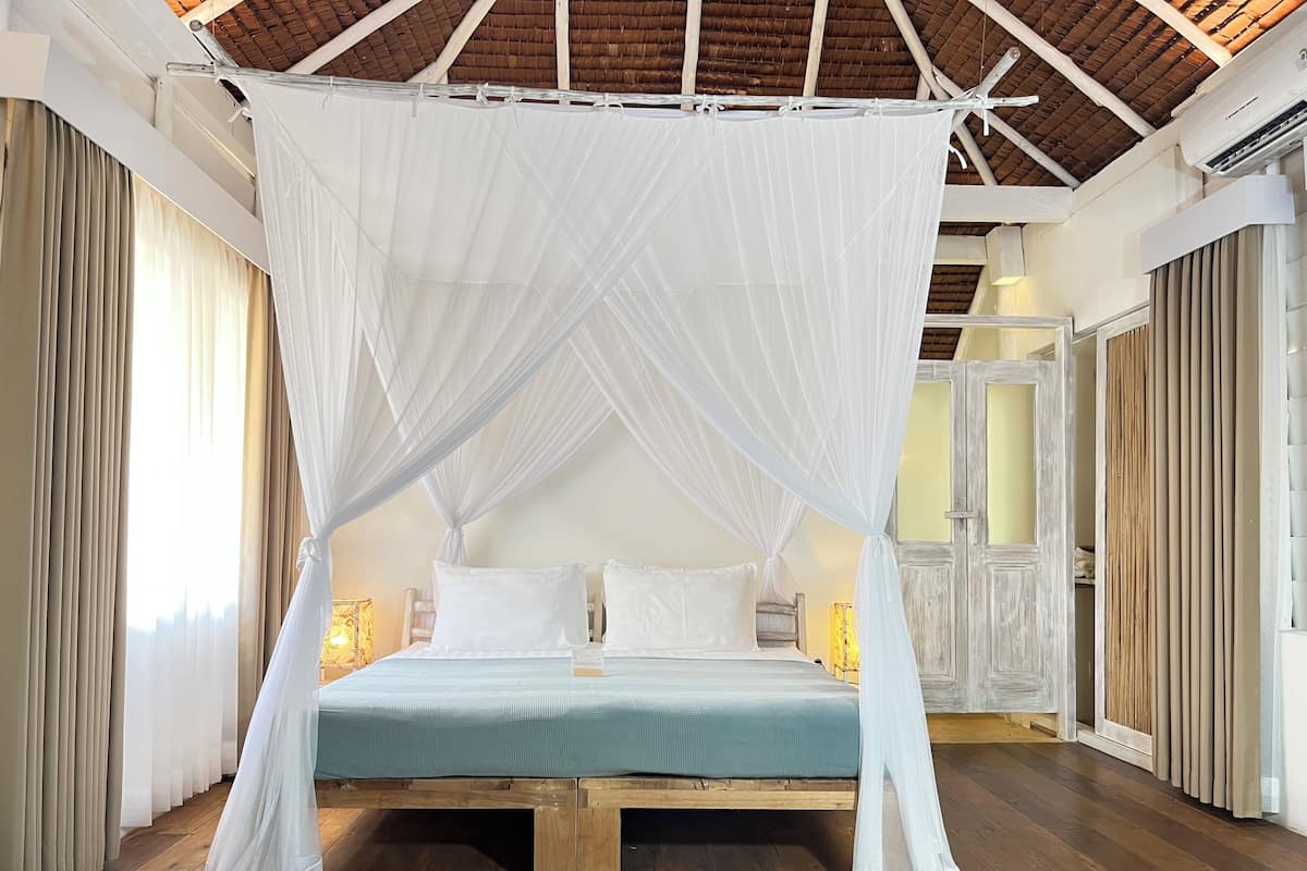 A room with a bed under a canopy, wooden flooring, and a rustic ceiling.