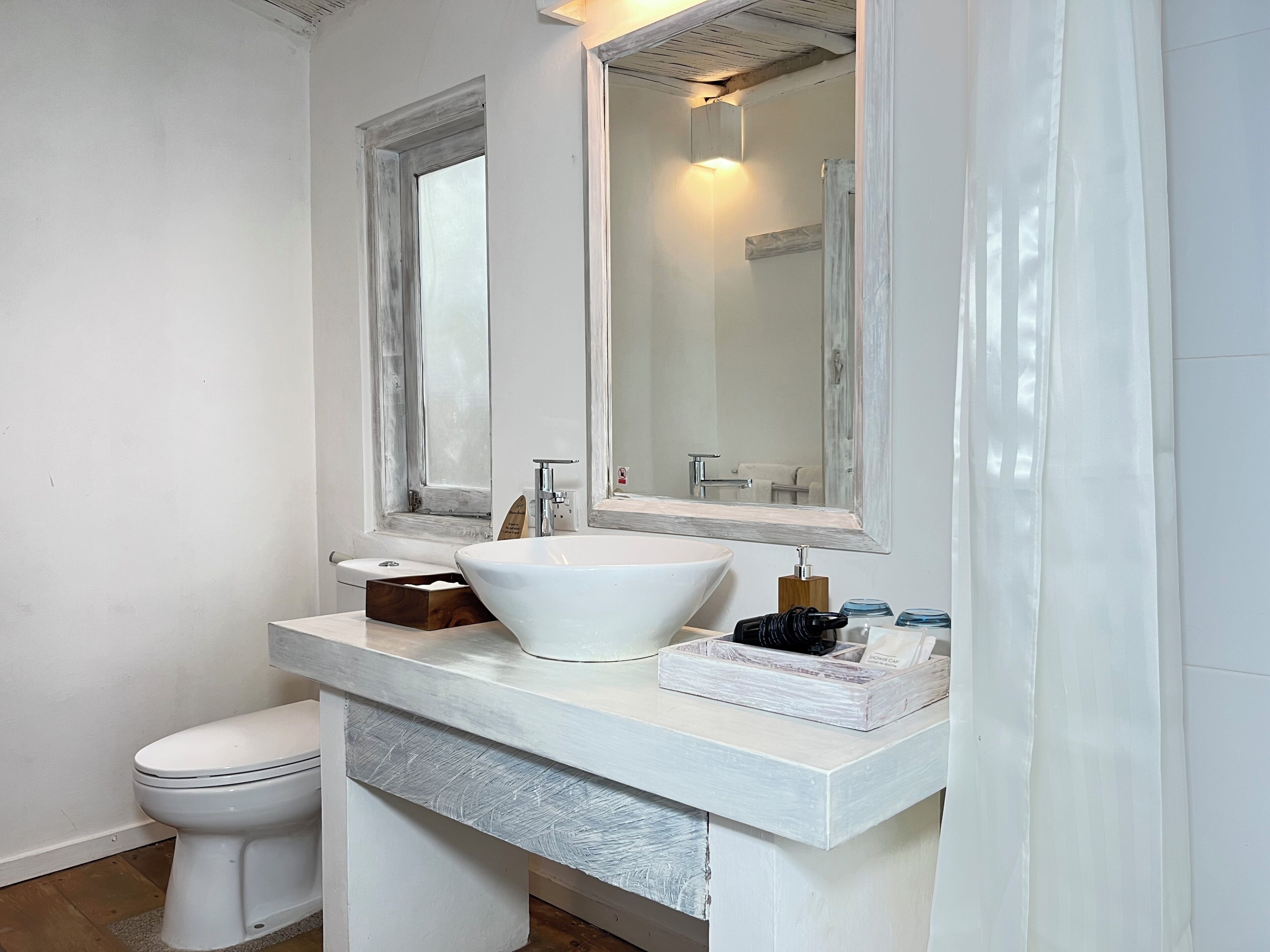 A bathroom with a white sink, a mirror, a toilet, and a window.