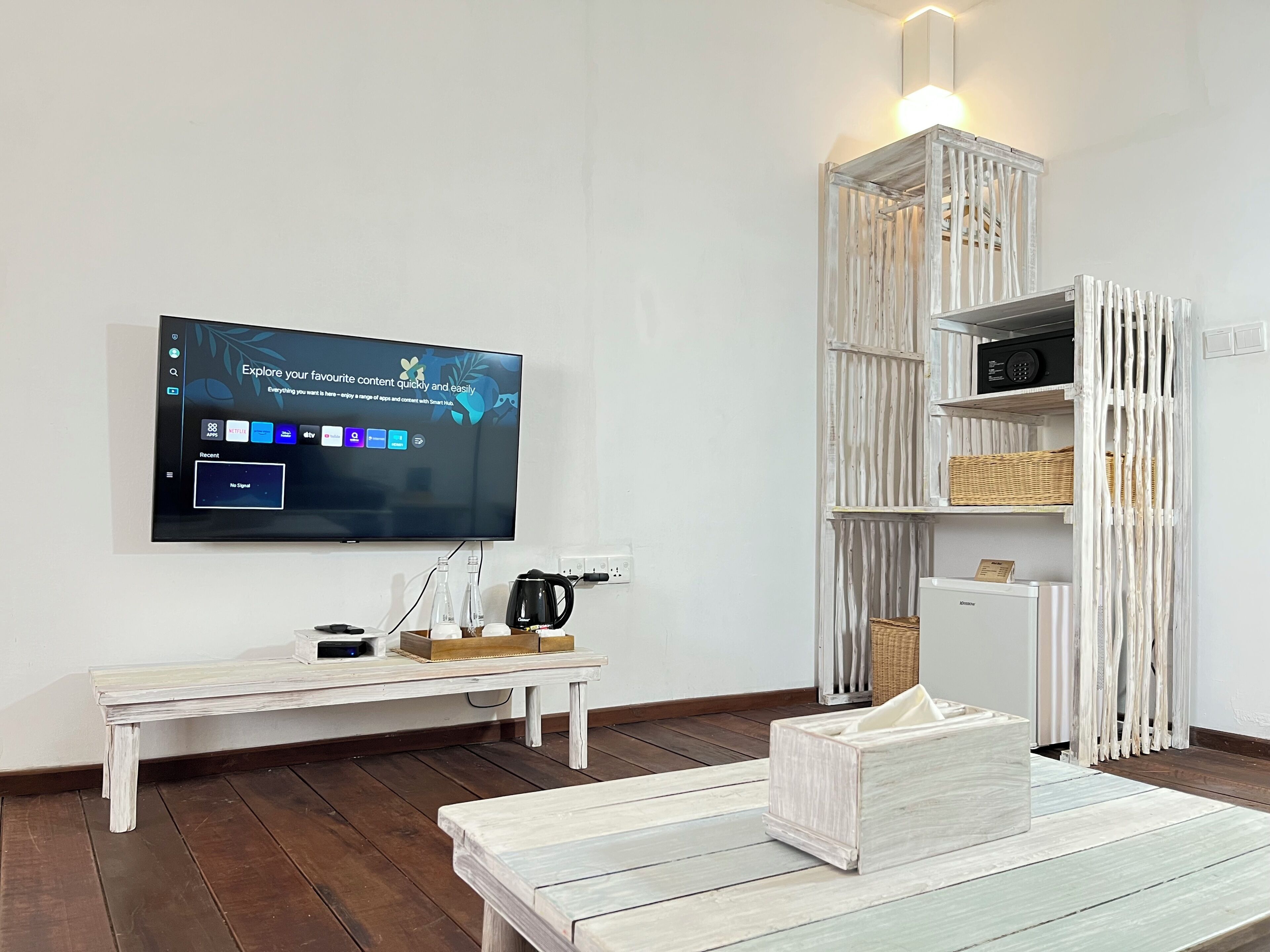 A modern living room with a flat-screen TV mounted on the wall, a white coffee table, a white bench, and a white-framed shelving unit with baskets.