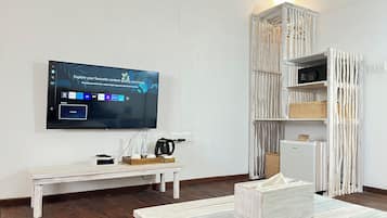 A modern living room with a flat-screen TV mounted on the wall, a white coffee table, a white bench, and a white-framed shelving unit with baskets.