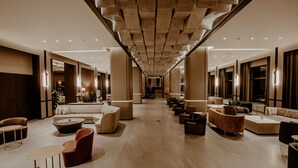 Un vestíbulo amplio con diseño moderno, que cuenta con una zona de estar central con sofás y sillones, y un techo alto con un patrón geométrico único.