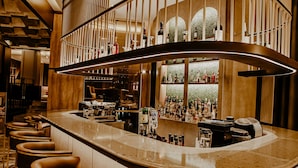 Un área de bar moderna con una barra curva, varios taburetes y una variedad de botellas y vasos.