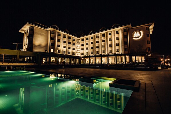 Un hotel con piscina, varios pisos y un logotipo destacado en la fachada.