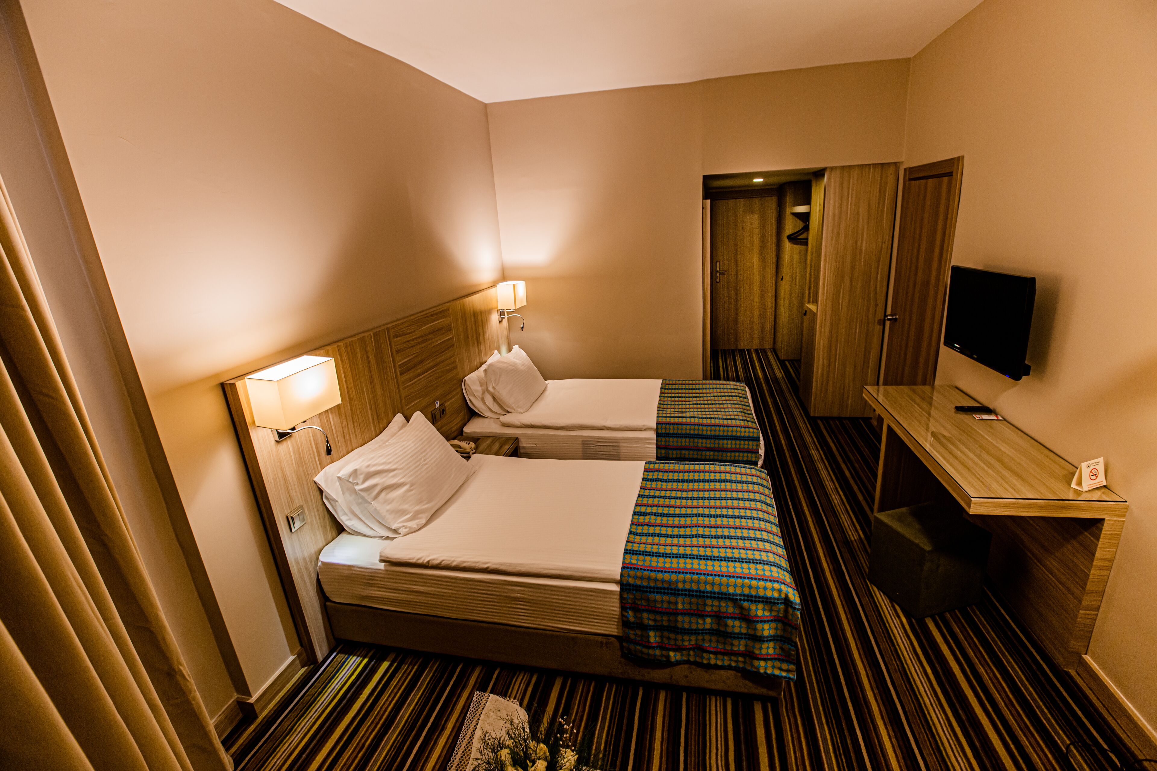 A hotel room with two beds, a TV, a desk, and a mirror.
