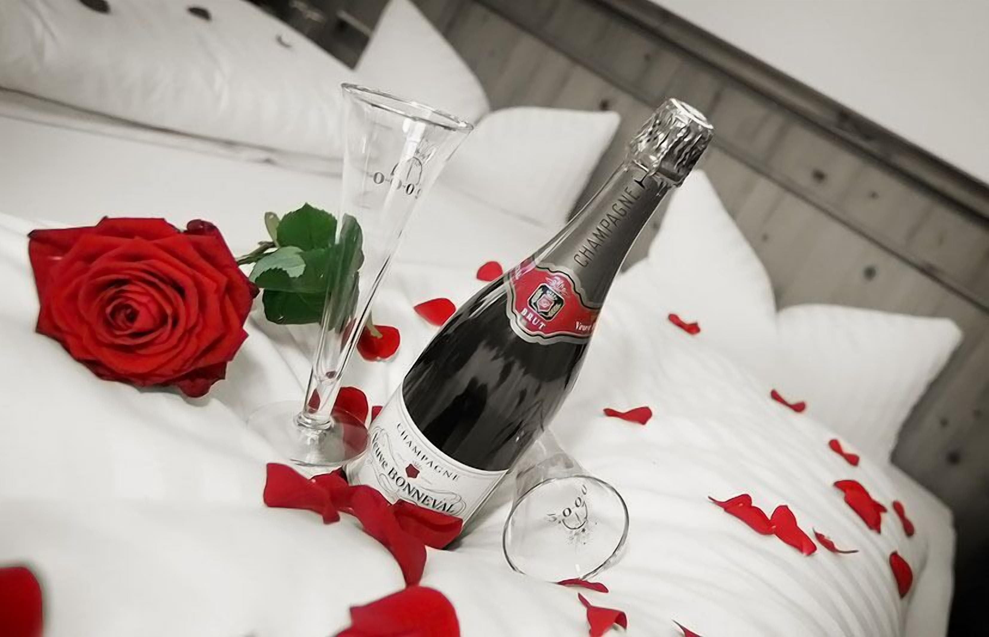 Een bed met een fles champagne, een glas en een roos.