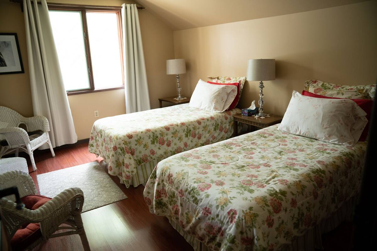 A hotel room with two beds, a chair, a nightstand, and a window with curtains.