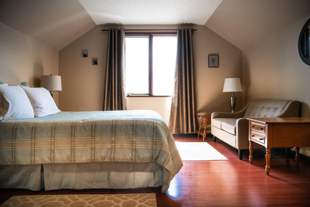 A bedroom with a bed, a chair, a nightstand, and a window.