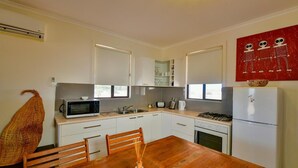 Una cocina compacta con gabinetes blancos, un microondas, una estufa y un refrigerador.
