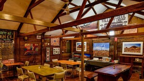 Un interior rústico con vigas de madera, mesas y sillas, decorado con obras de arte y un letrero del Hotel William Creek.