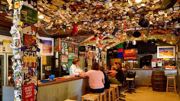 Un bar con mostrador de madera, taburetes y varios carteles y letreros en las paredes.