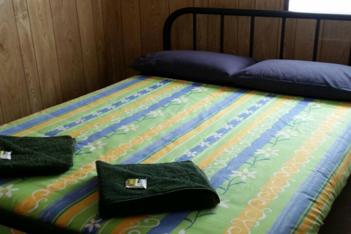 Een eenpersoonsbed met een kleurrijke gestreepte spreidek en twee kussens, evenals twee opgevouwen handdoeken op het bed.