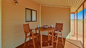 Un espacio de estar al aire libre con techo, sillas y mesa de madera, una ventana y vistas al desierto.