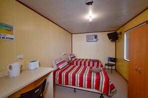 Een kleine, compacte kamer met twee bedden, een bureau, een stoel, een televisie en een airconditioning.