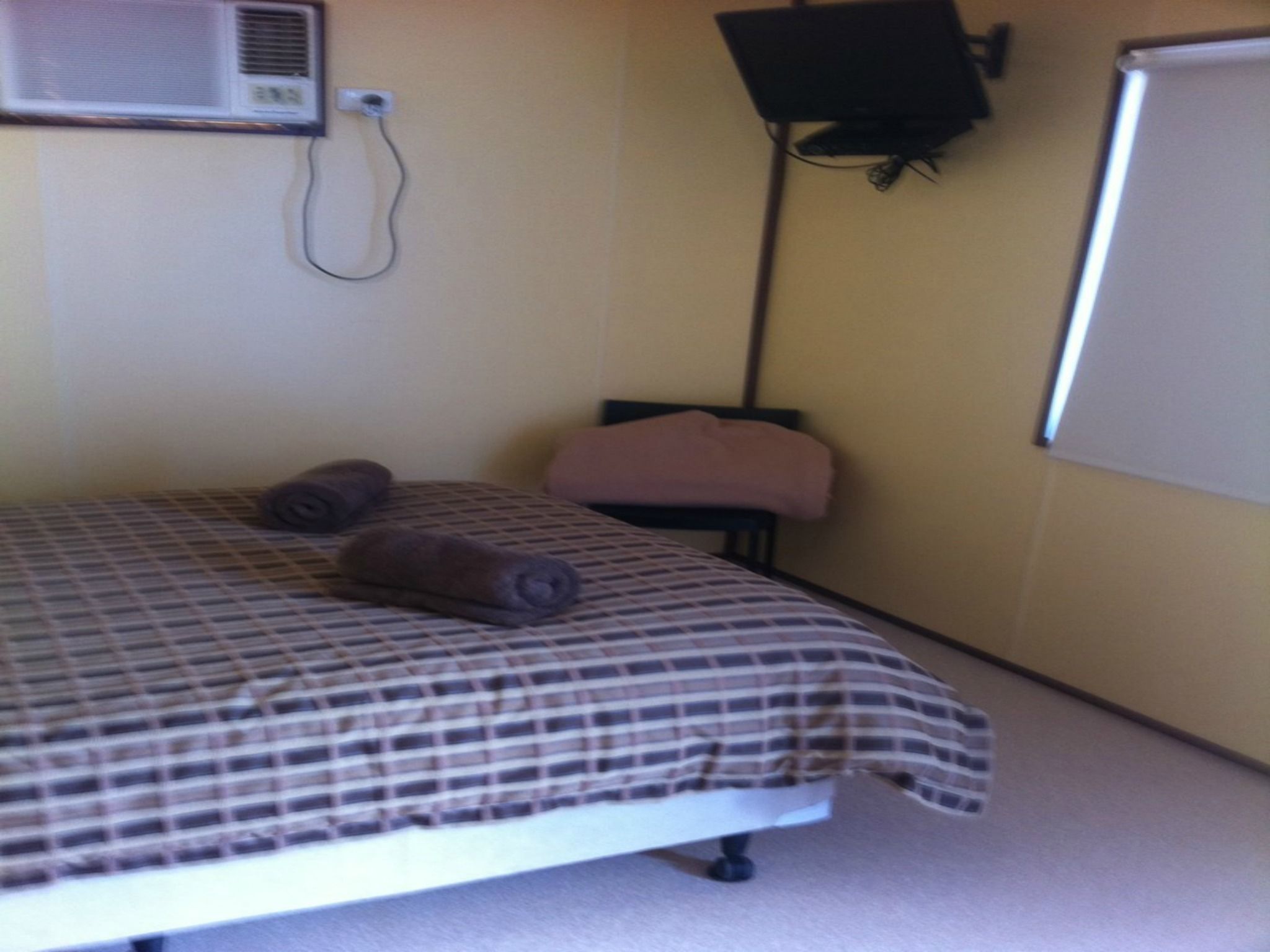 A room with a bed, a wall-mounted air conditioner, a television, and a whiteboard.