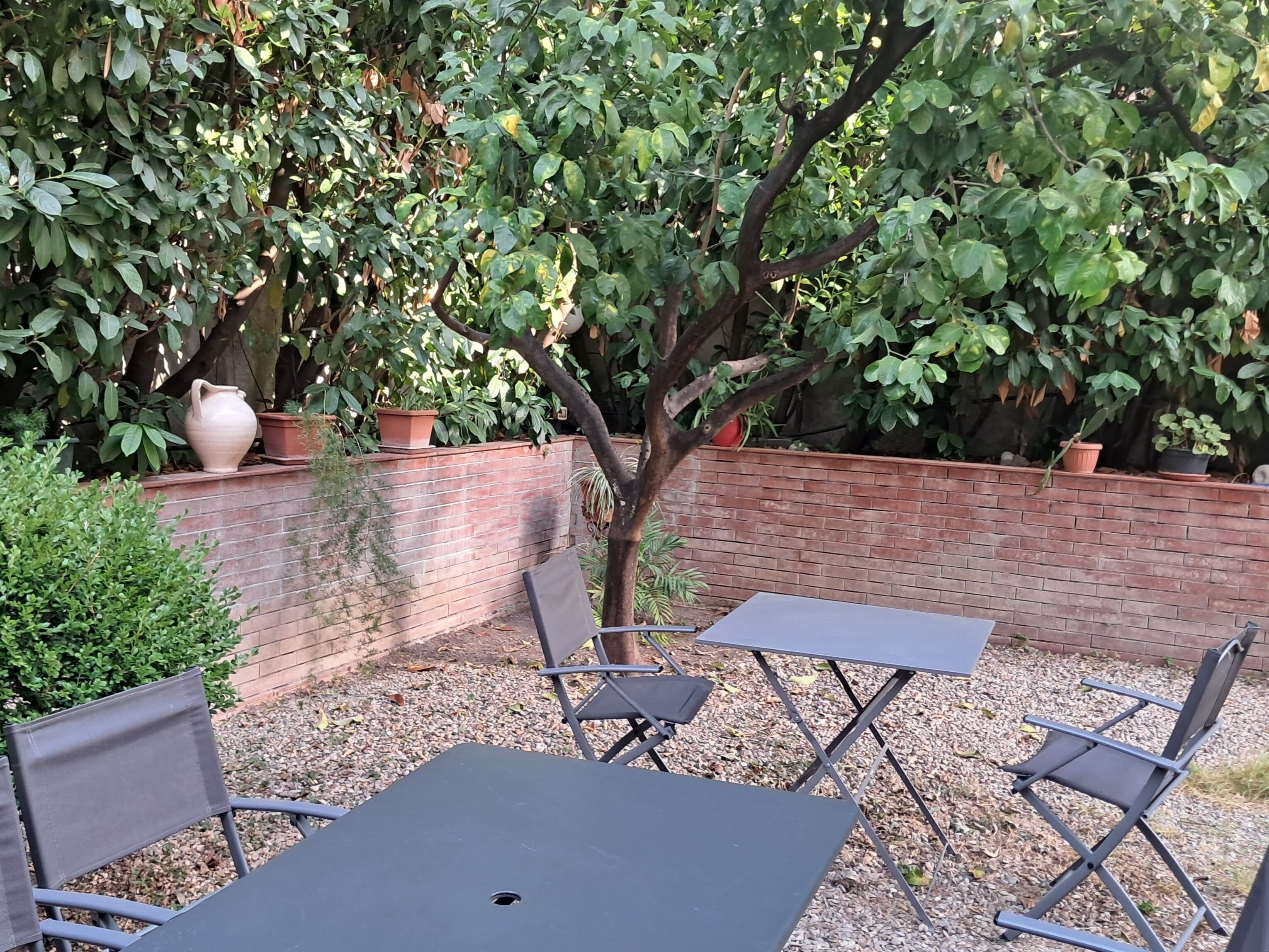 An outdoor seating area with a brick wall, potted plants, and a tree.
