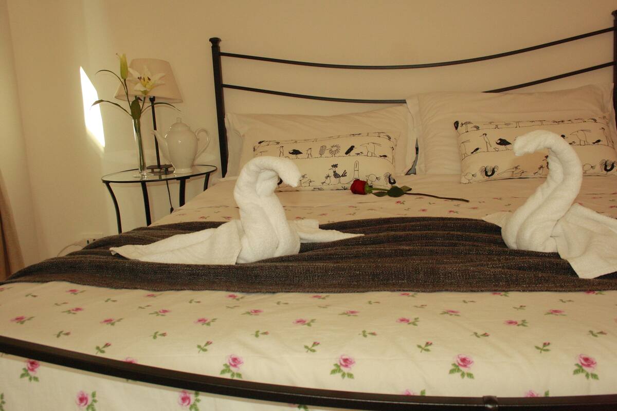 A bed with a floral bedspread, a rose, and two towels shaped like swans.